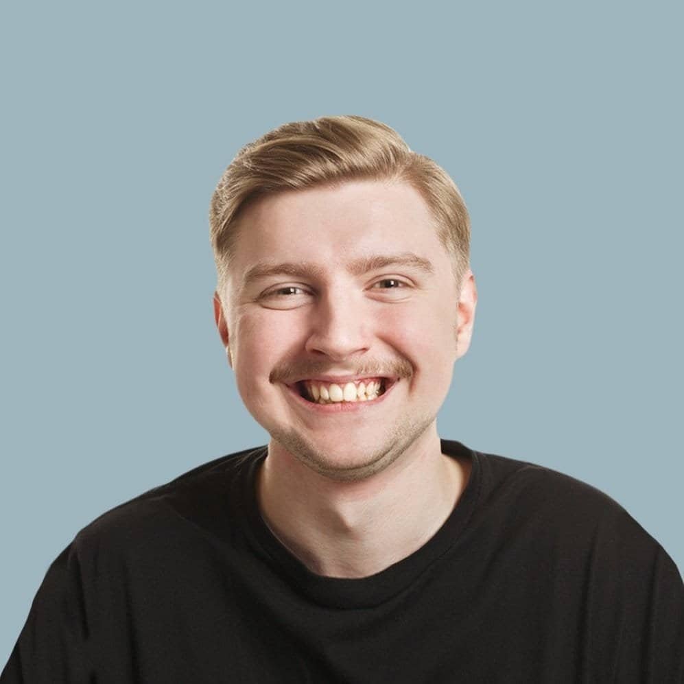 Cheerful young man smiling, wearing a black t-shirt, against a light blue background.
