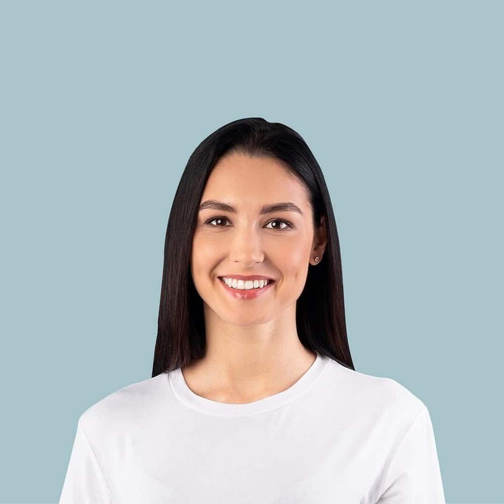 Smiling woman with long dark hair, wearing a white shirt, on a light blue background.