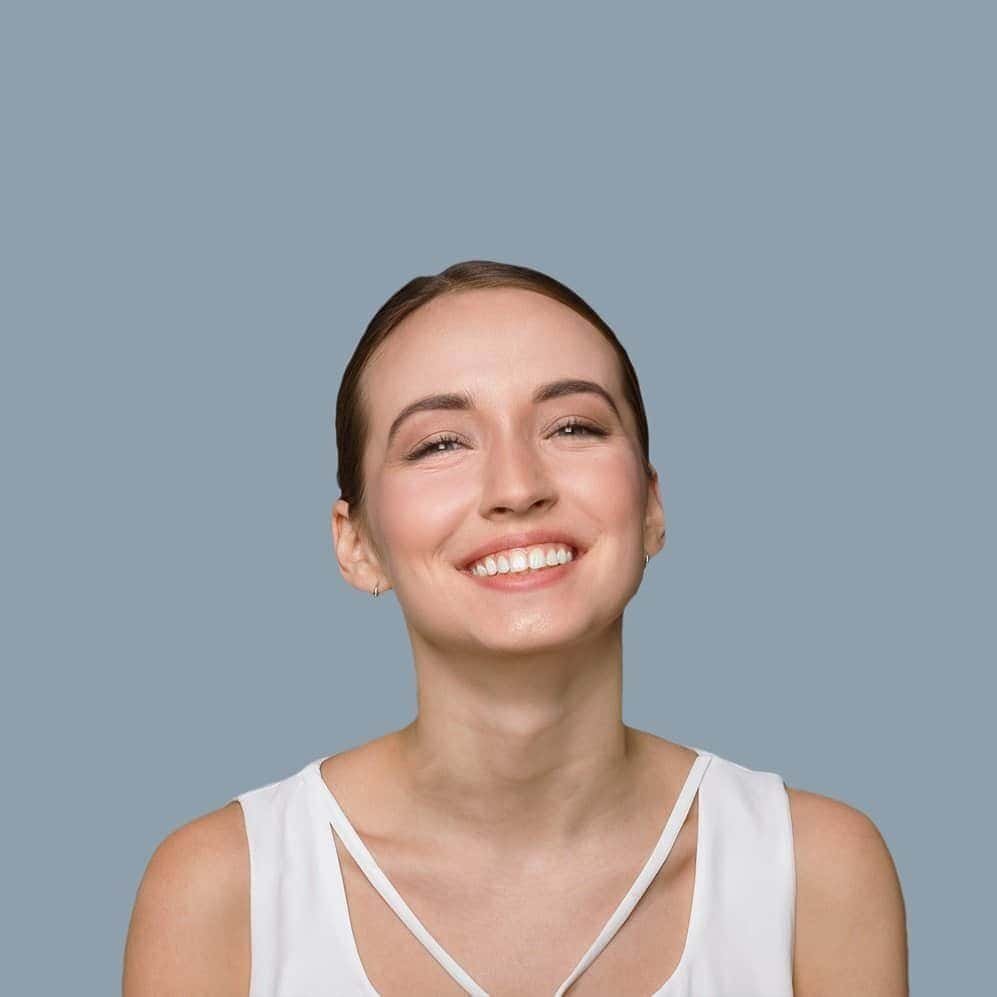 Woman smiling with a bright, cheerful expression, wearing a white top against a blue background.